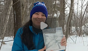 Jessica is standing in snow-filled woods with a copy of the book