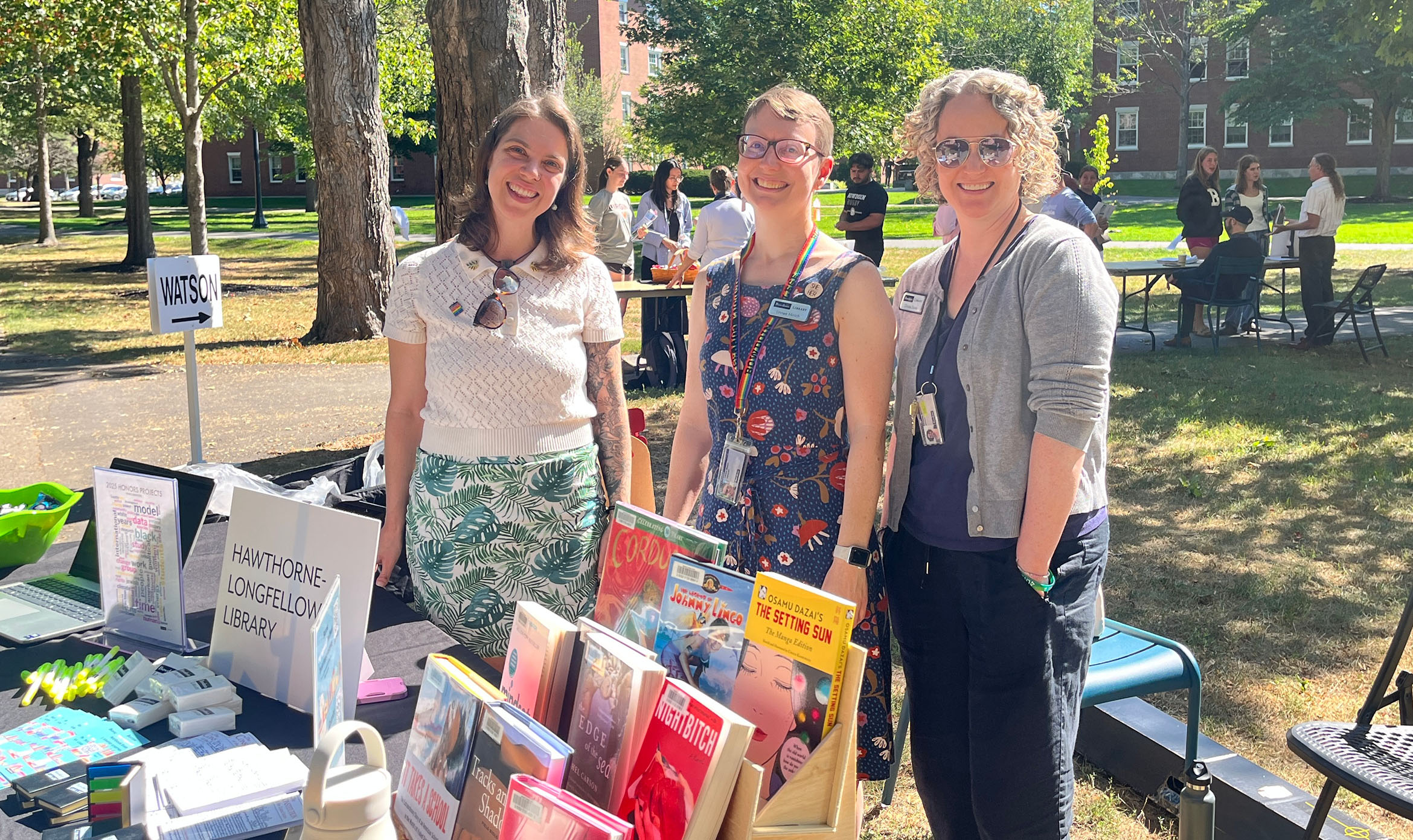 Anna, Linnea, and Christie, staff members of Bowdoin Library, smiling while standing by the library's Academic Fair table
